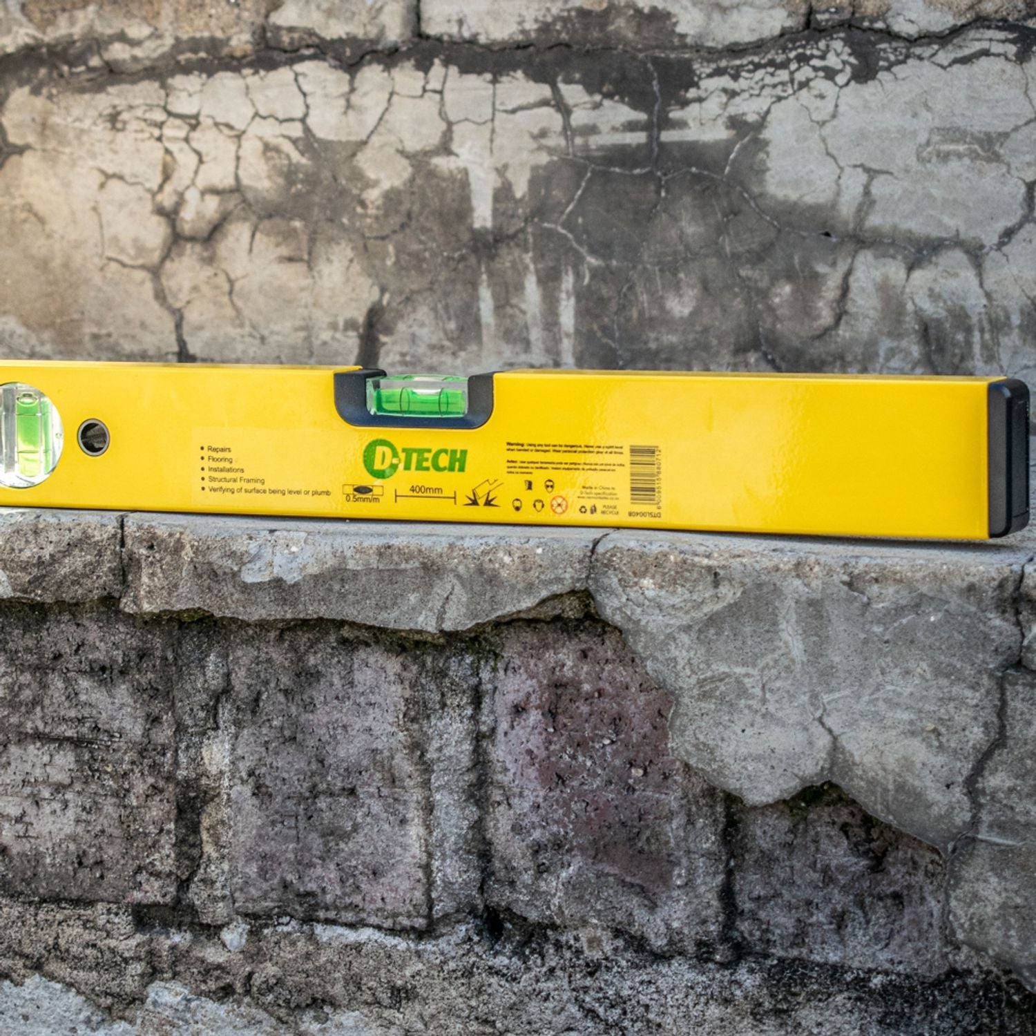 Yellow spirit level with green vial lying on stone wall surface