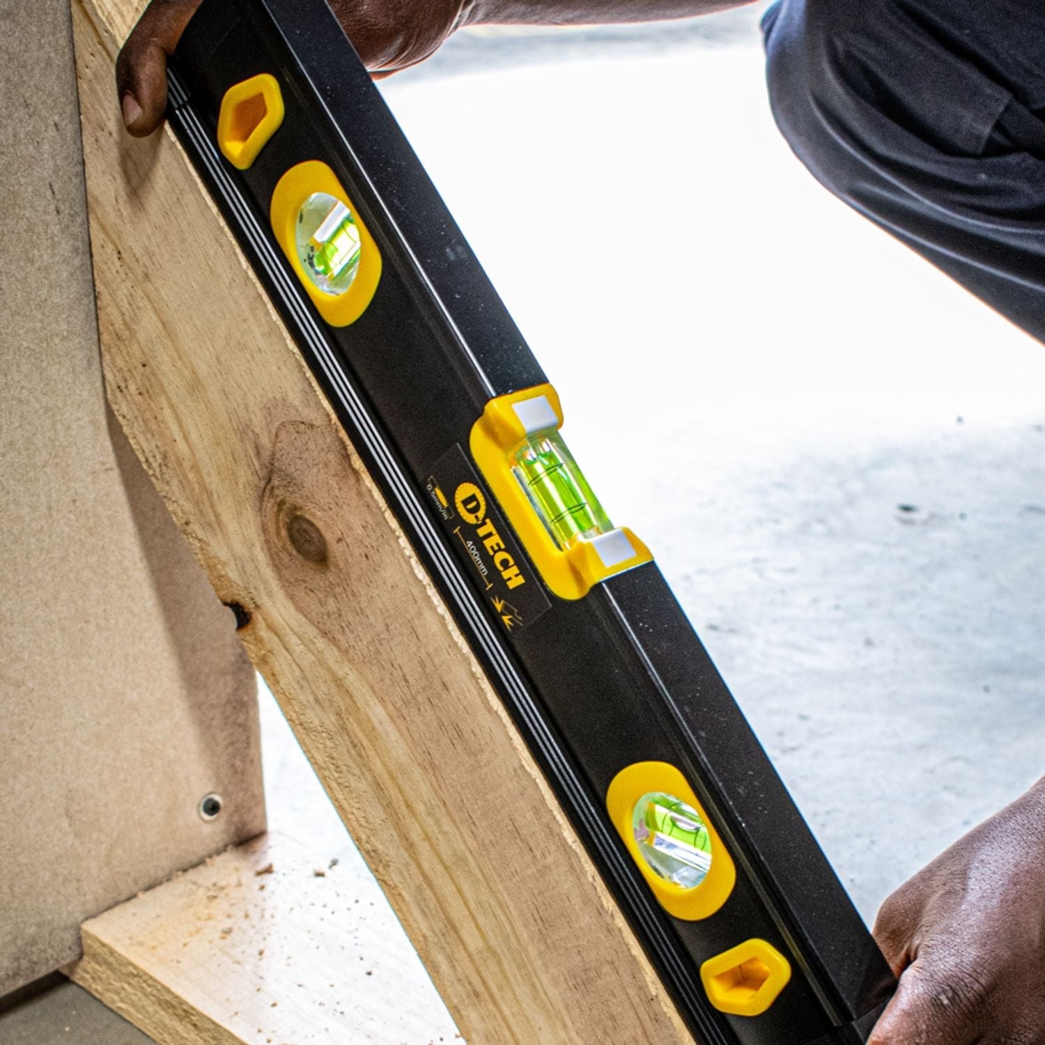Spirit level on wood beam with yellow bubble vials, black aluminium housing