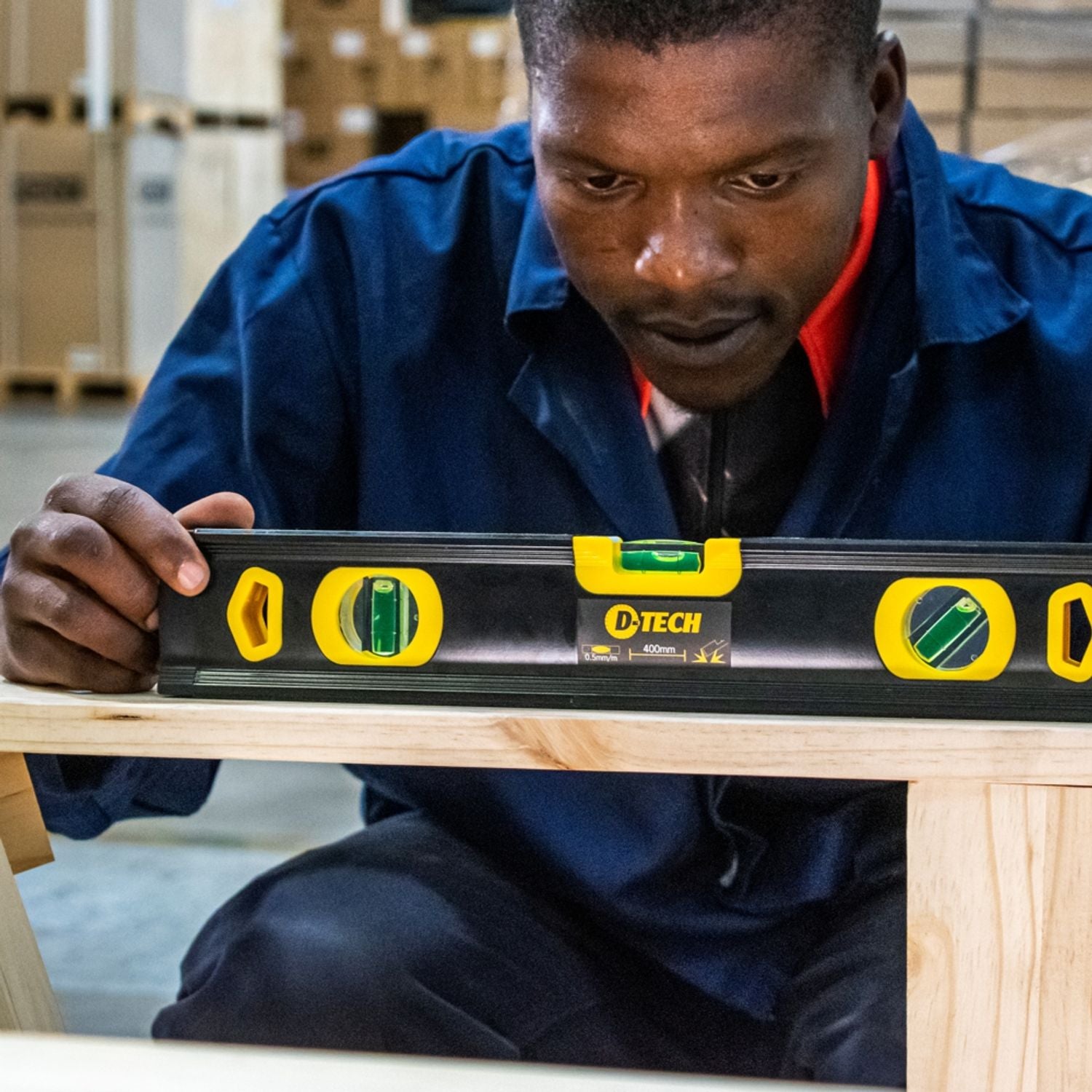 Worker holding a 400mm spirit level across a wooden beam, yellow bubble vials