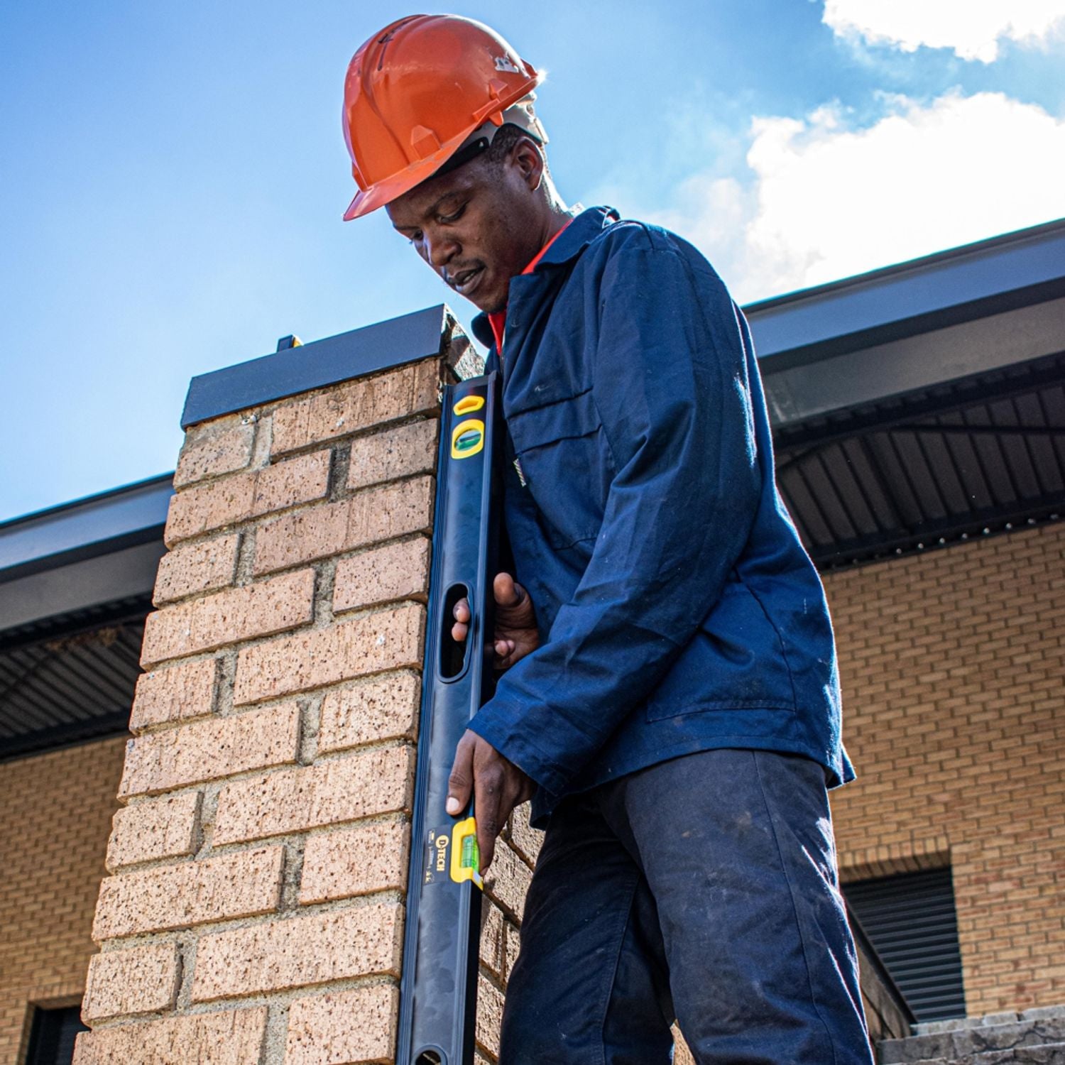 Worker using a spirit level against a brick wall, black body with yellow vials