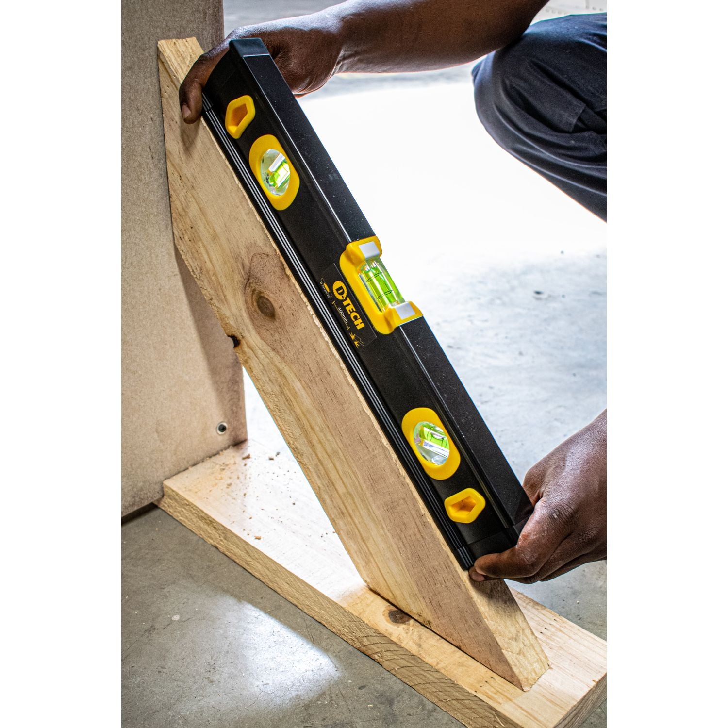 Black spirit level beam with yellow vials resting on a wooden board